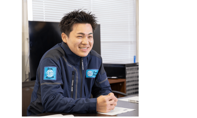 オフィスのデスクに座り、充実した表情で微笑む若い男性スタッフ
