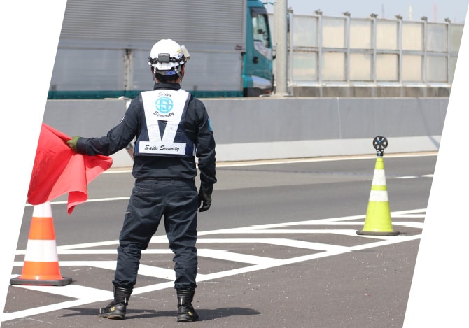 高速道路上で赤い旗を持ち交通規制をおこなう警備スタッフ