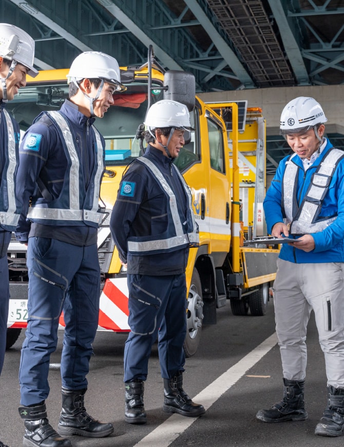 高速道路下で責任者の説明を受ける社員たち