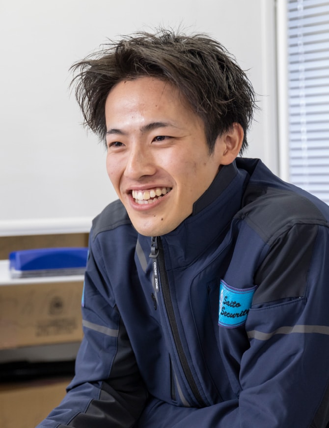 紺色の作業着姿で笑顔で受け答えをする若手の男性社員